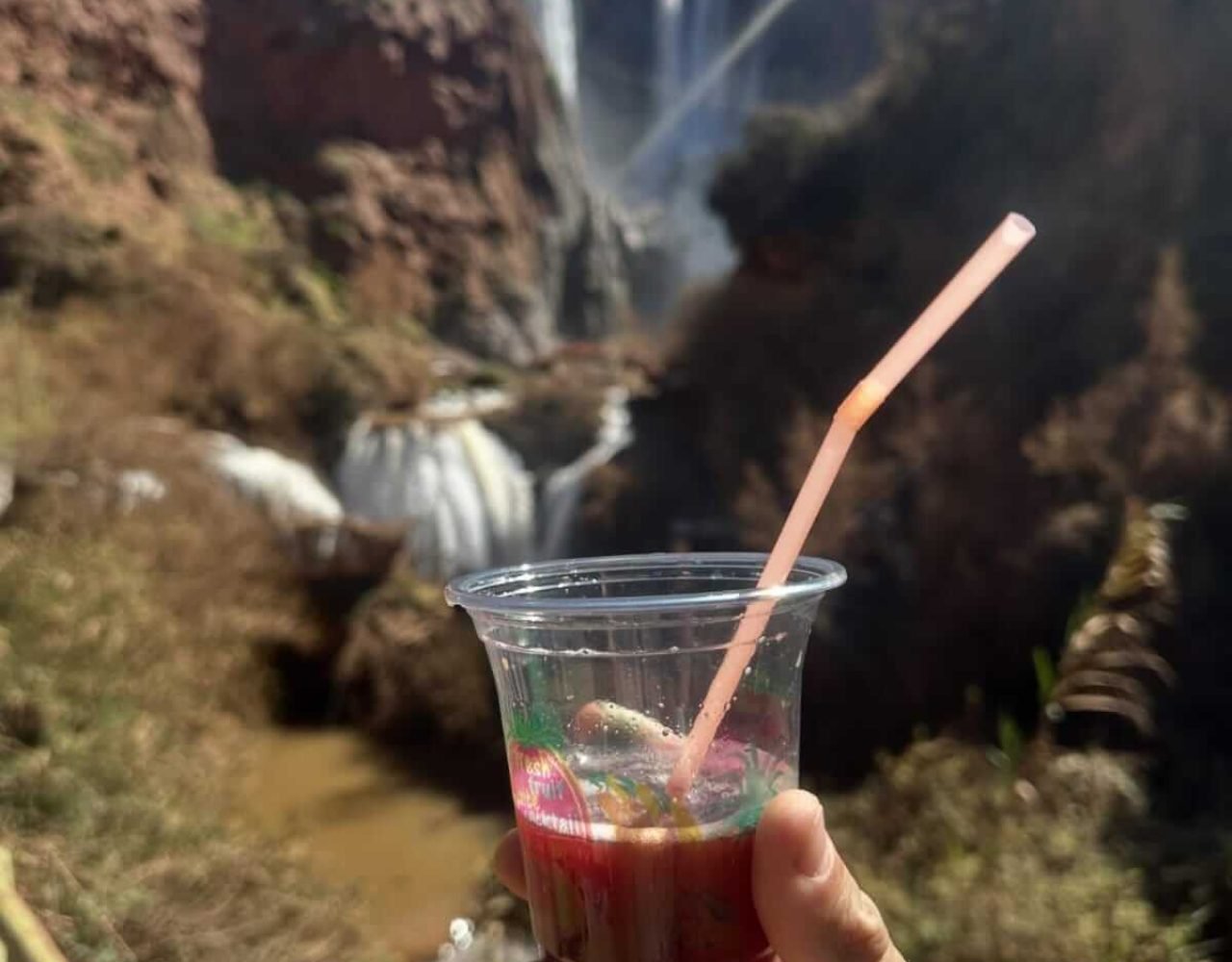 Hand holding a refreshing drink with Ouzoud Falls in the background