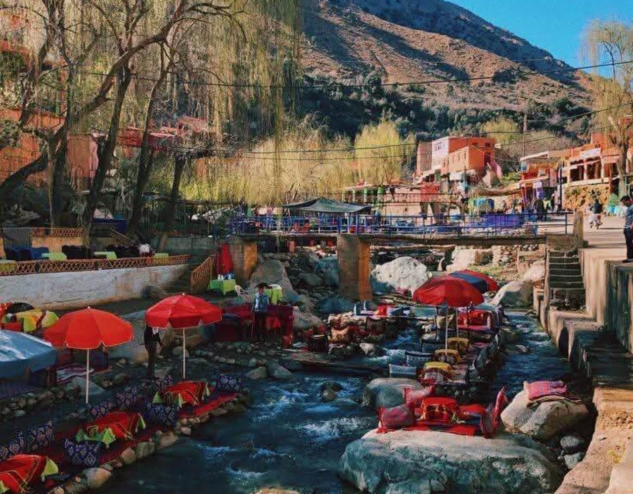 Seating areas with red umbrellas over Ourika river surrounded by mountains